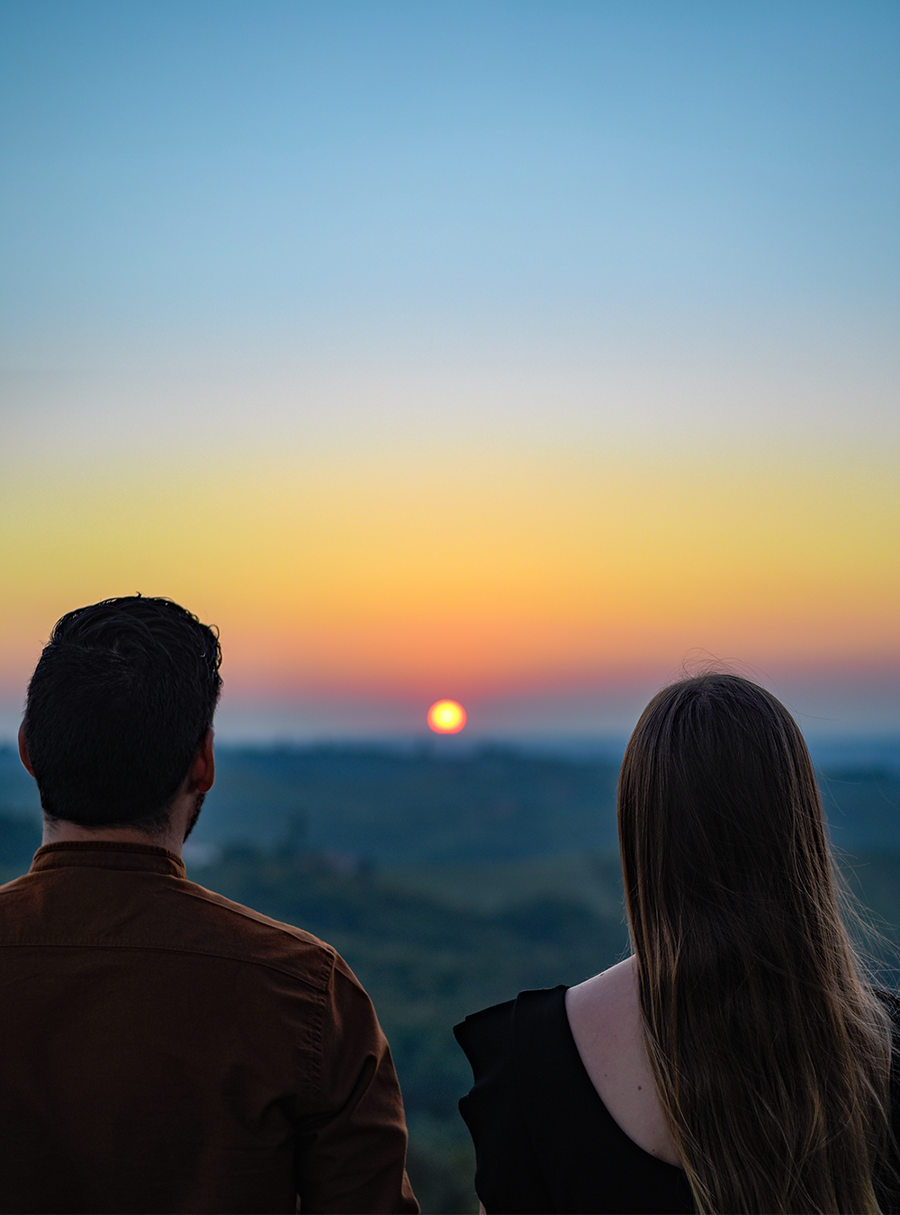 Casal de costas contemplando o pôr do sol sobre as colinas