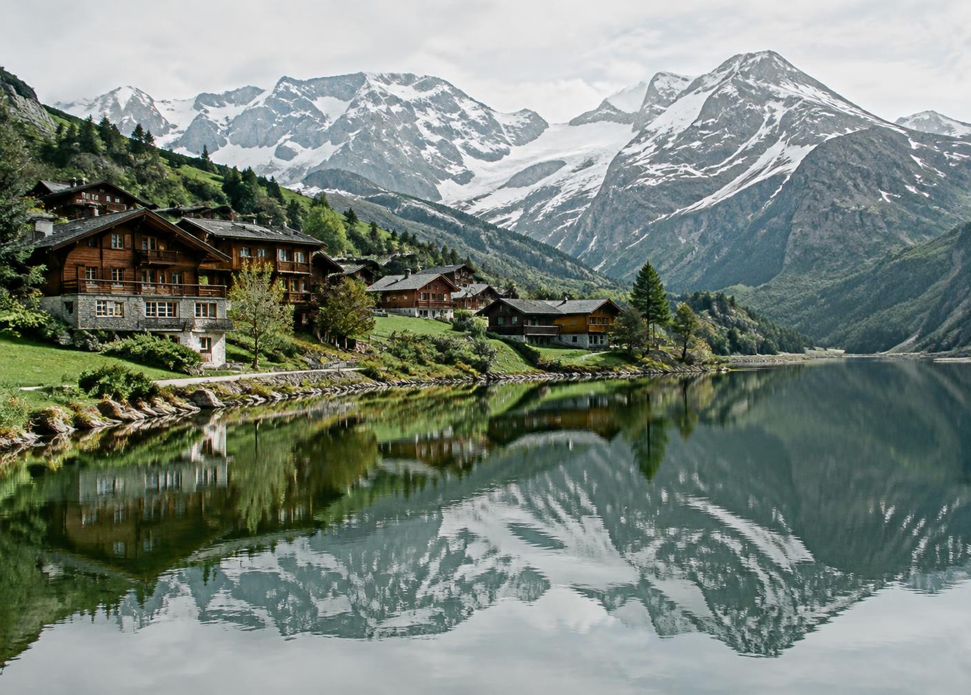 Vilarejo alpino de chalés de madeira refletido em lago calmo com montanhas nevadas